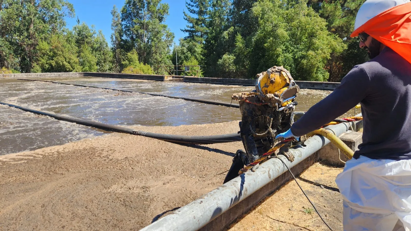Buzo industrial de C&R saliendo de una piscina de tratamiento de aguas, asistido desde el borde por un compañero